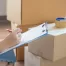 Fatboy Slims Moving Company | Blog Person checks a list on a clipboard while seated beside stacked cardboard boxes. Packing tape is nearby.