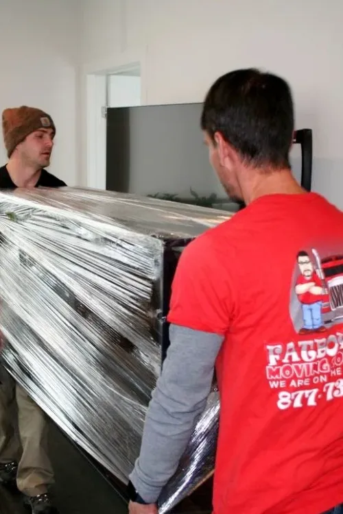 Fatboy Slims movers carrying wrapped furniture inside a Colorado Springs home.