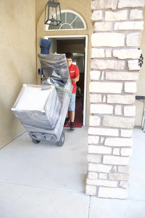 Fatboy Slims Moving Company mover transporting wrapped furniture out of a home.
