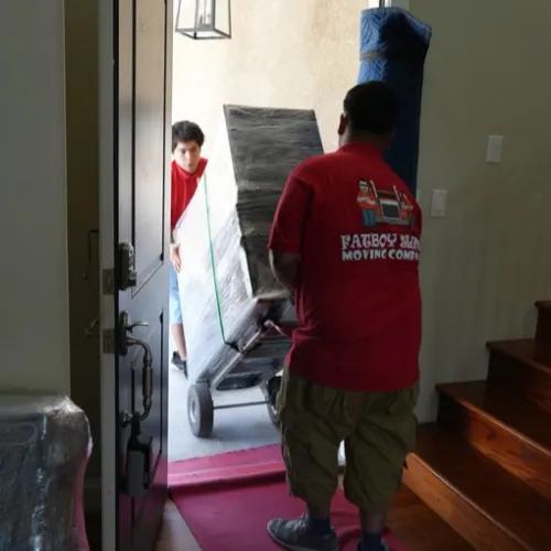 Fatboy Slims Moving Company movers carrying wrapped furniture into a home.
